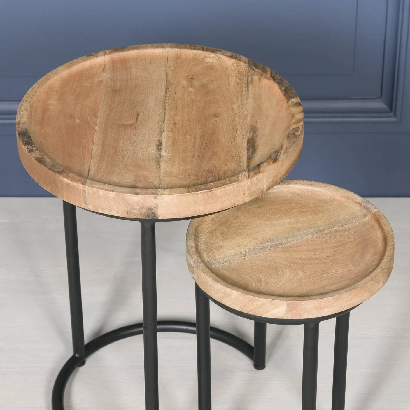 Set of two round wooden nesting tables with black metal legs against blue wall
