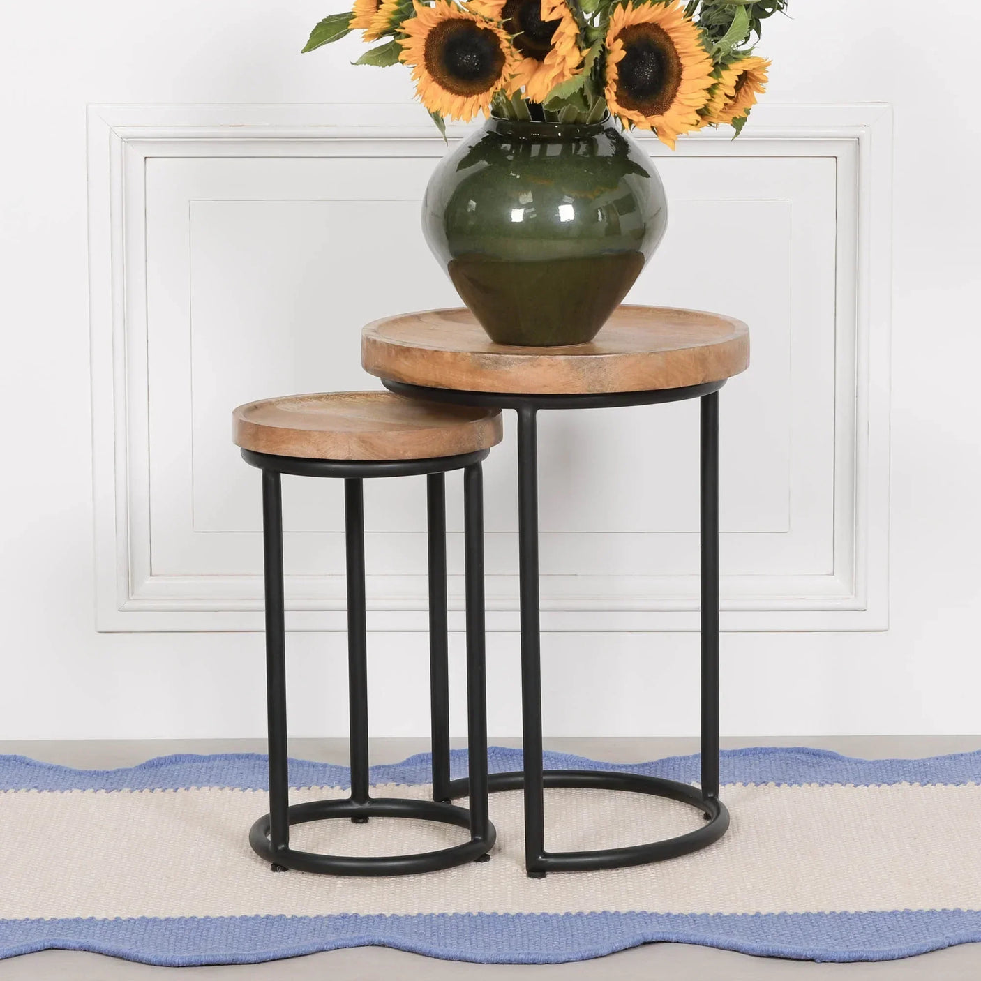 Set of two round nesting tables with wood tops and black metal legs, vase with sunflowers