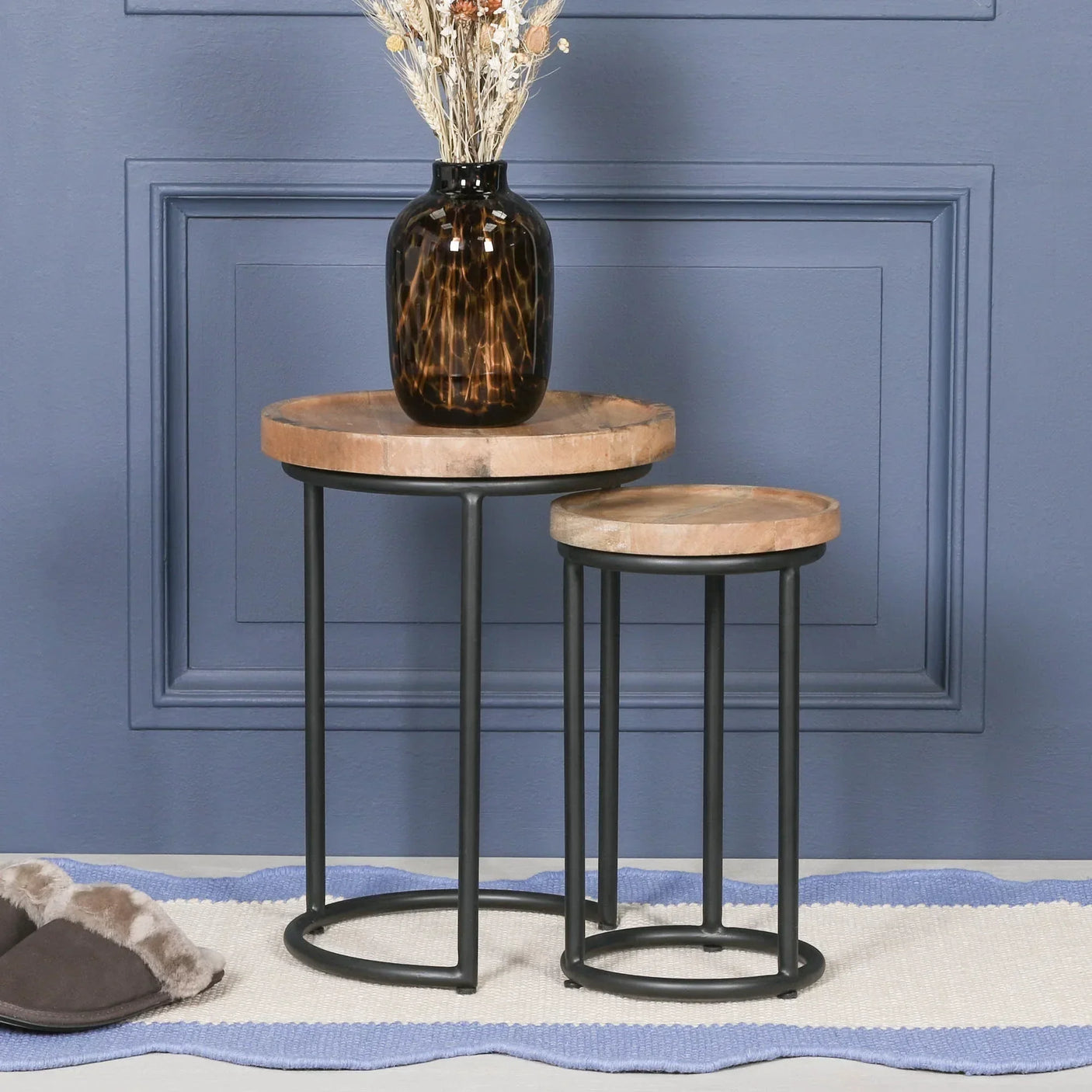 Set of two round wooden nesting tables with black metal frames against blue wall