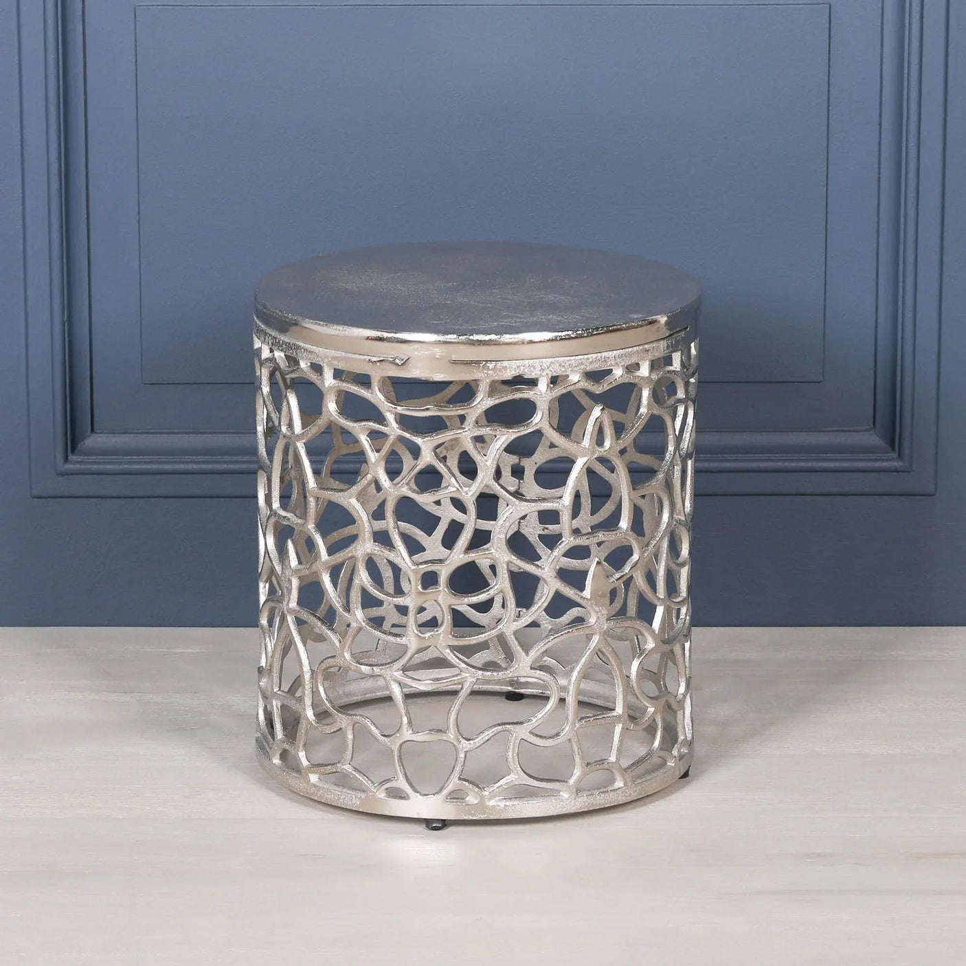 Silver metal side table with abstract cut-out pattern on light wood floor