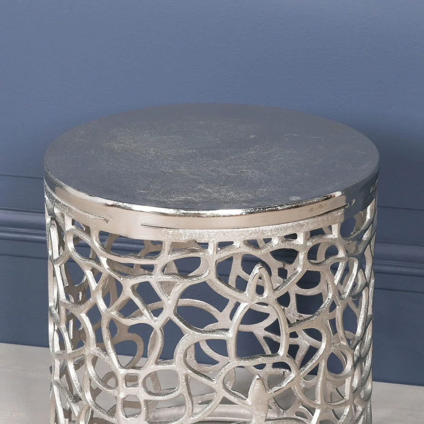 Silver metal side table with intricate openwork design against blue wall