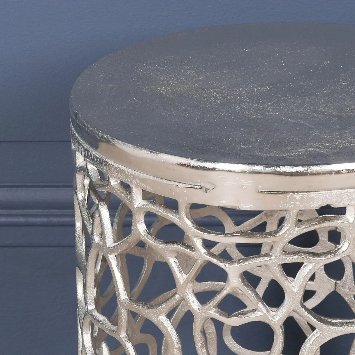 Silver metal side table with round top and openwork lattice frame against blue wall