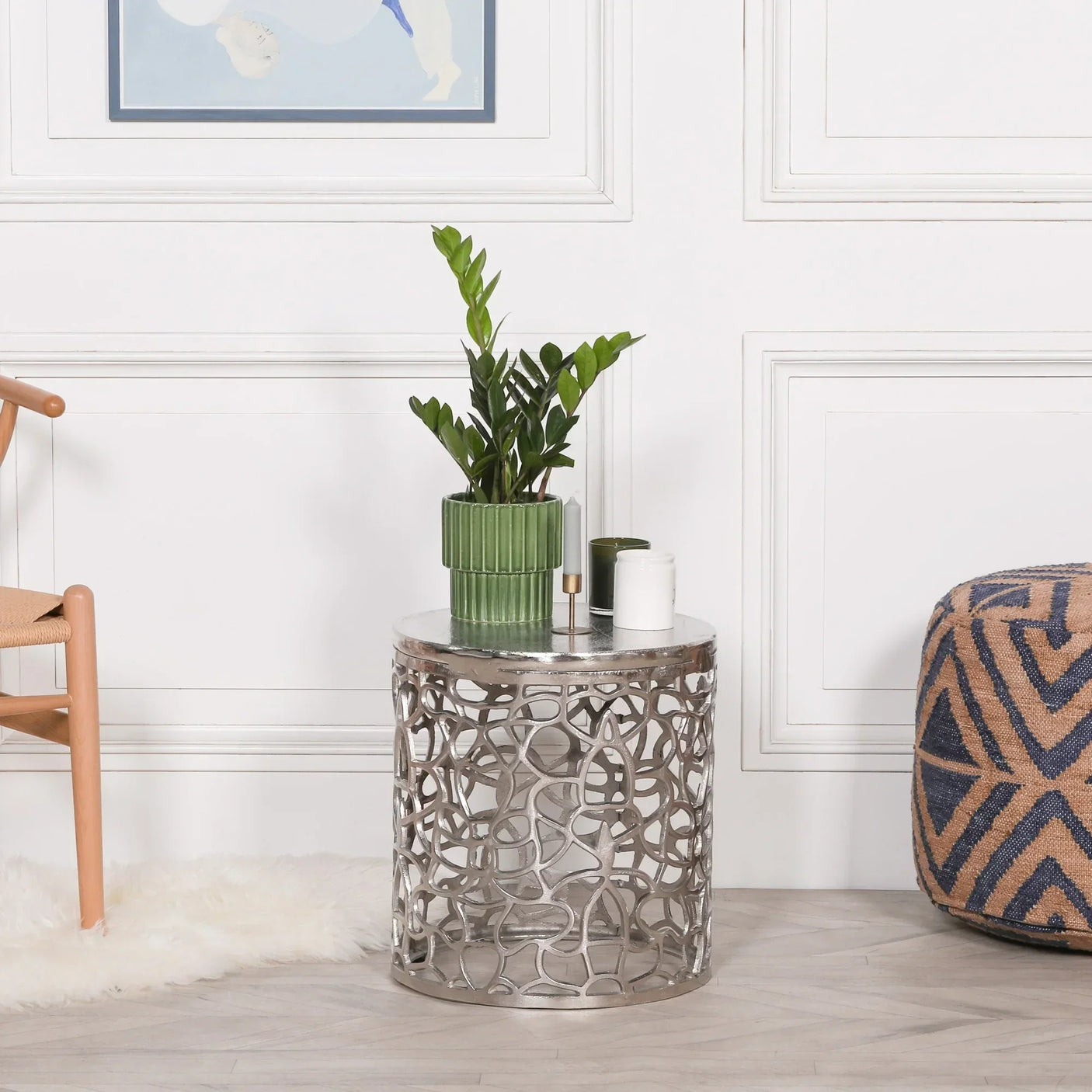Silver metal side table with cut-out design, topped with green plant and candles