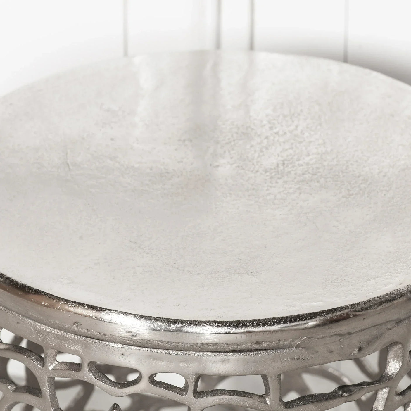 Closeup of silver metal side table top with textured surface and openwork base design