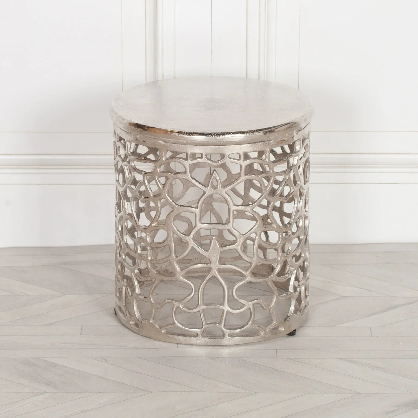Silver metal side table with decorative cut-out pattern on wood floor