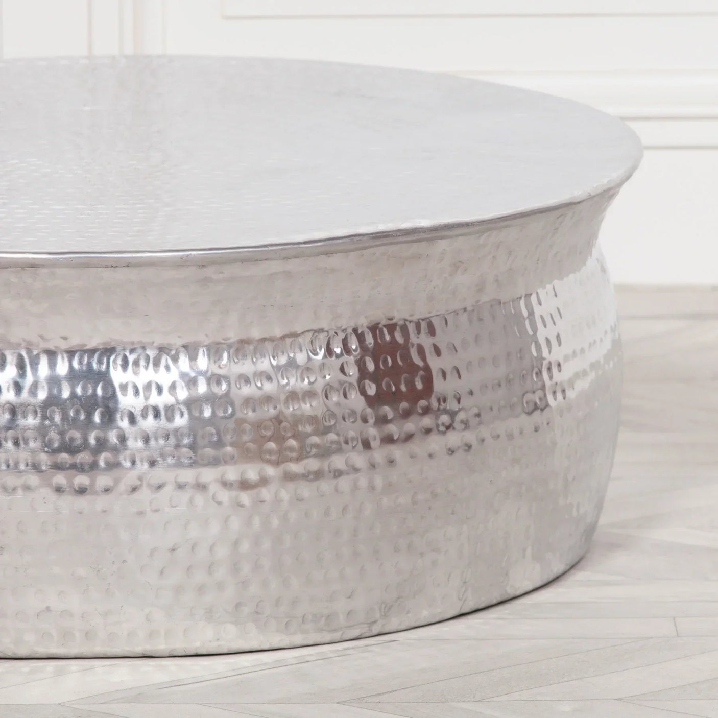 Round hammered metal coffee table with silver finish on light wood floor