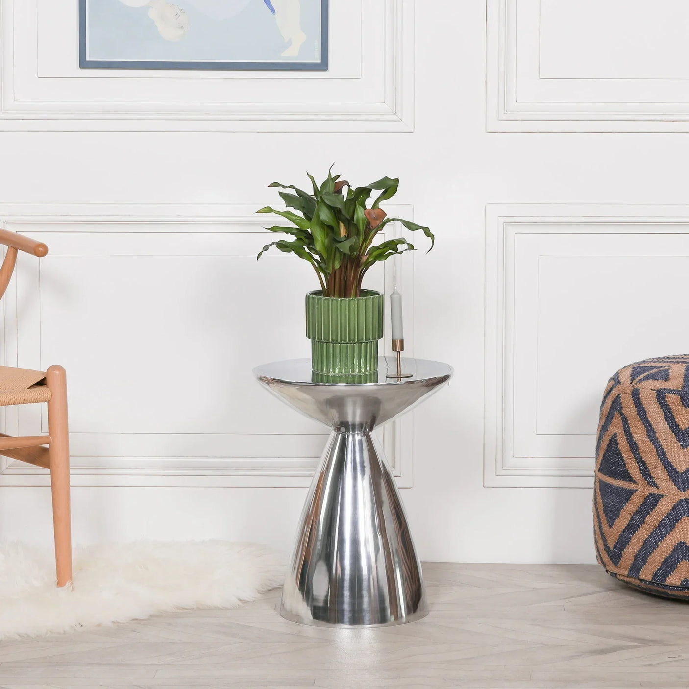 Silver metal side table with green plant and candle, styled in modern living room setting