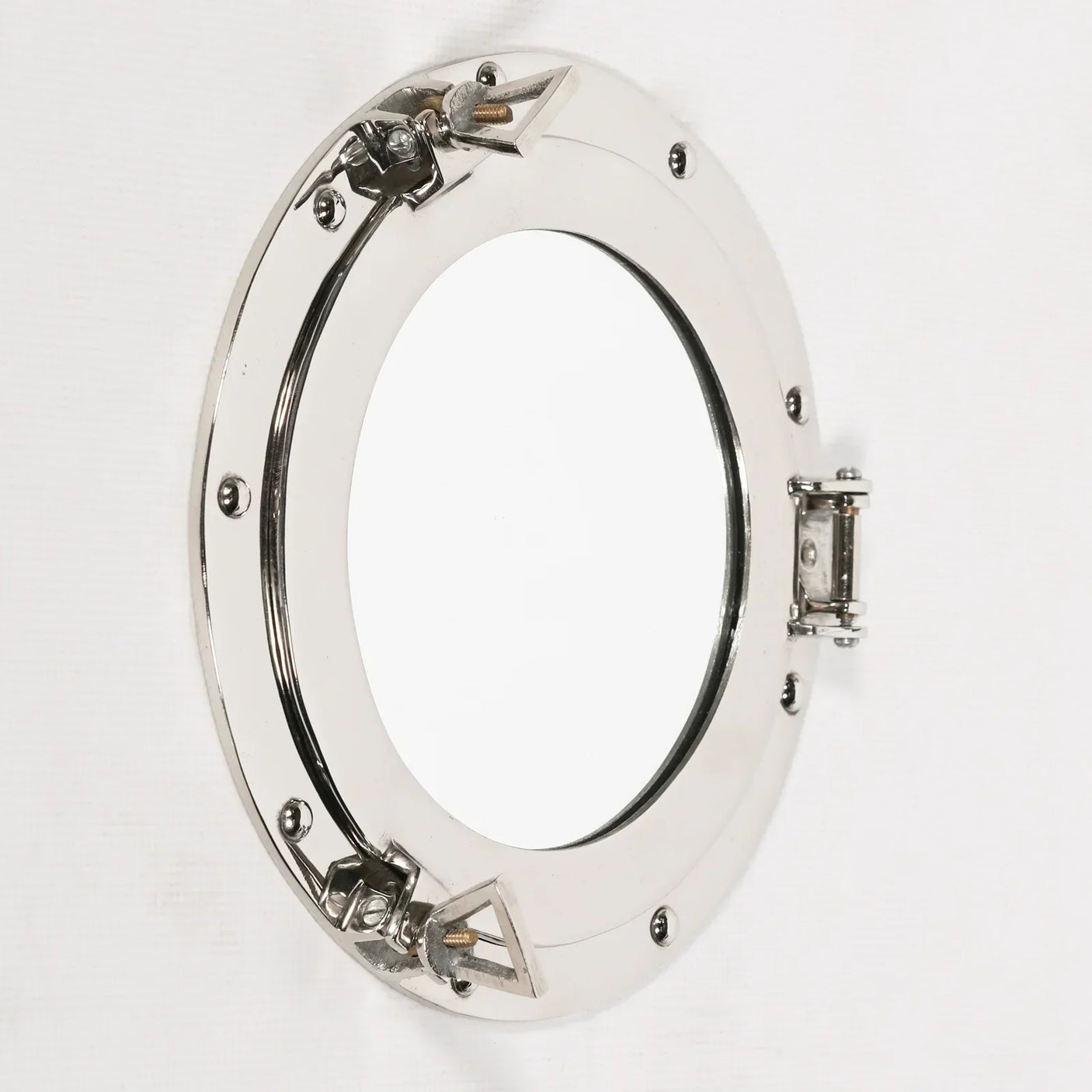 Polished chrome porthole mirror with round frame and hinge detail on white wall