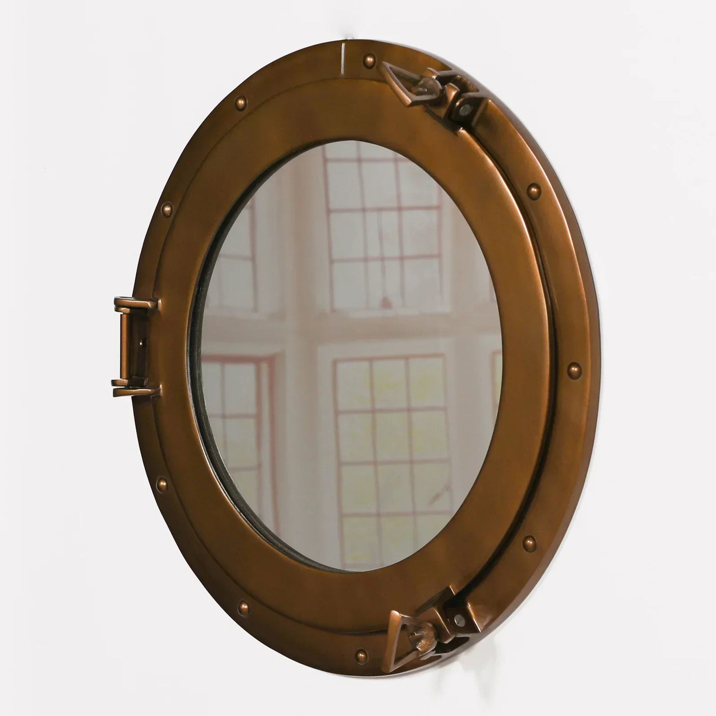 Round bronze porthole mirror with metal frame and latch detail on white wall