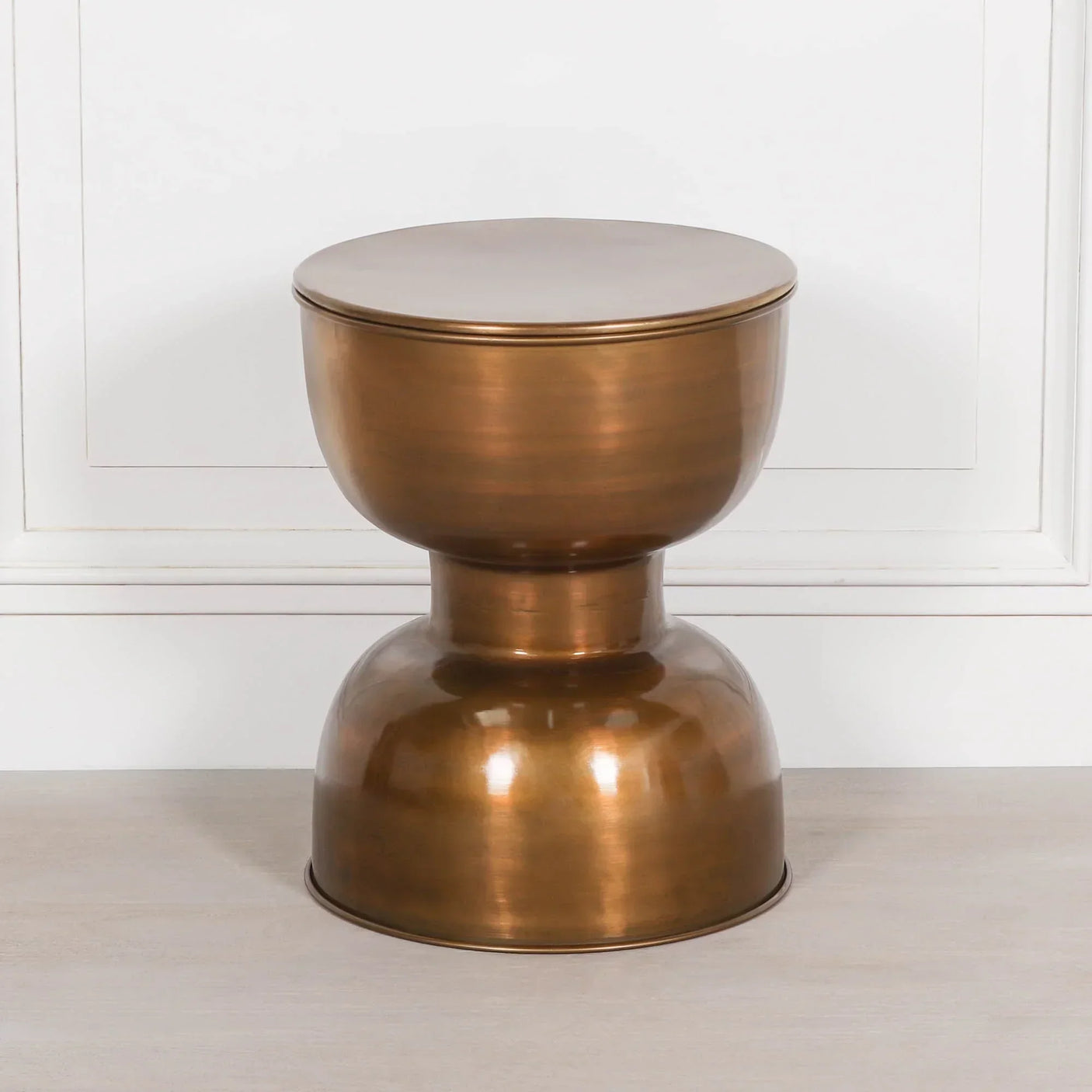 Bronze metal side table with round top and curved base on light wood floor