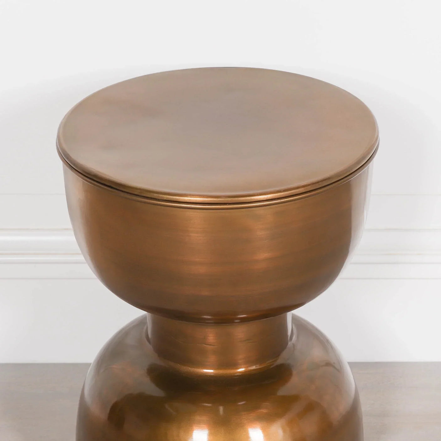 Round bronze metal side table with smooth finish against white wall