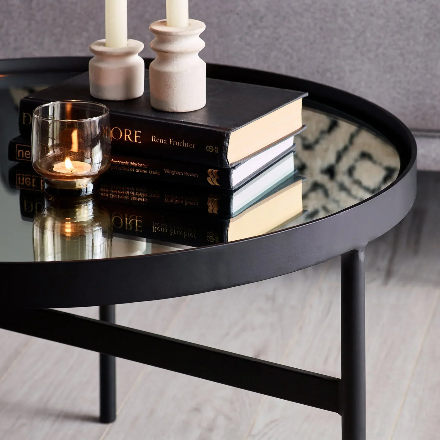 Round mirror glass coffee table with black metal frame, books, candles, and tealight holder