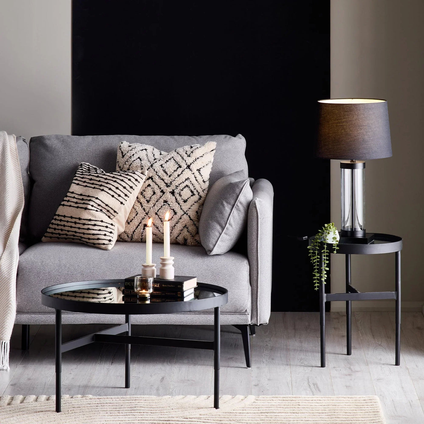 Grey fabric sofa with patterned cushions, black round coffee table and side table with lamp