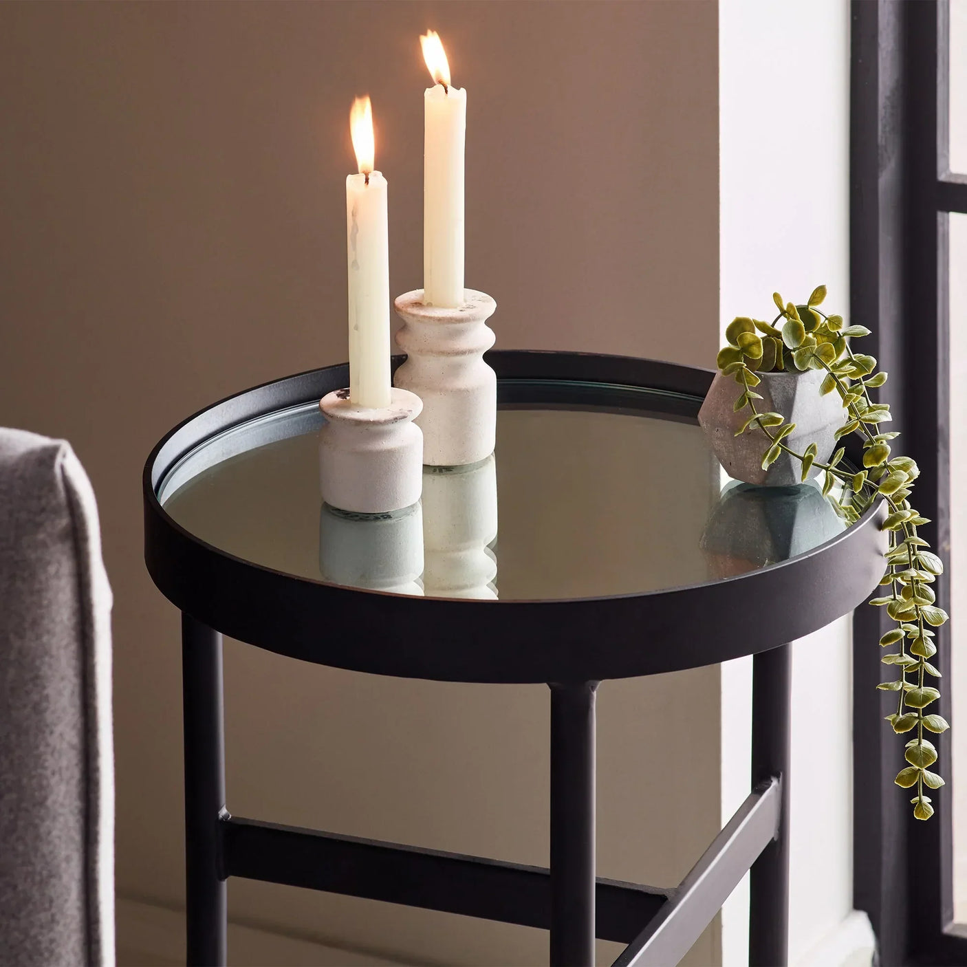 Round glass lamp table with black metal frame, two candles, and small plant decor