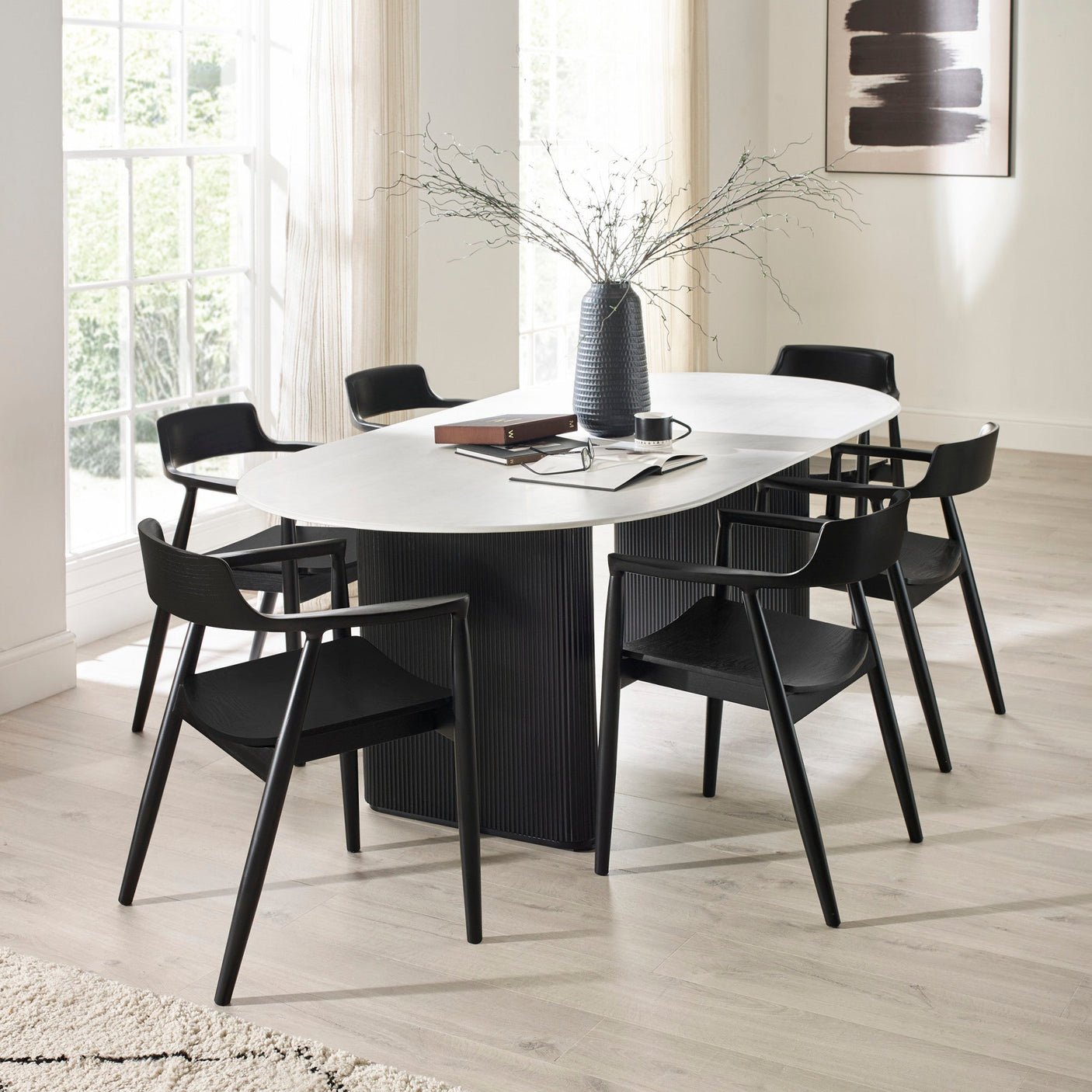 Six black wooden dining chairs with curved backs around white oval dining table in room with light flooring and decor.