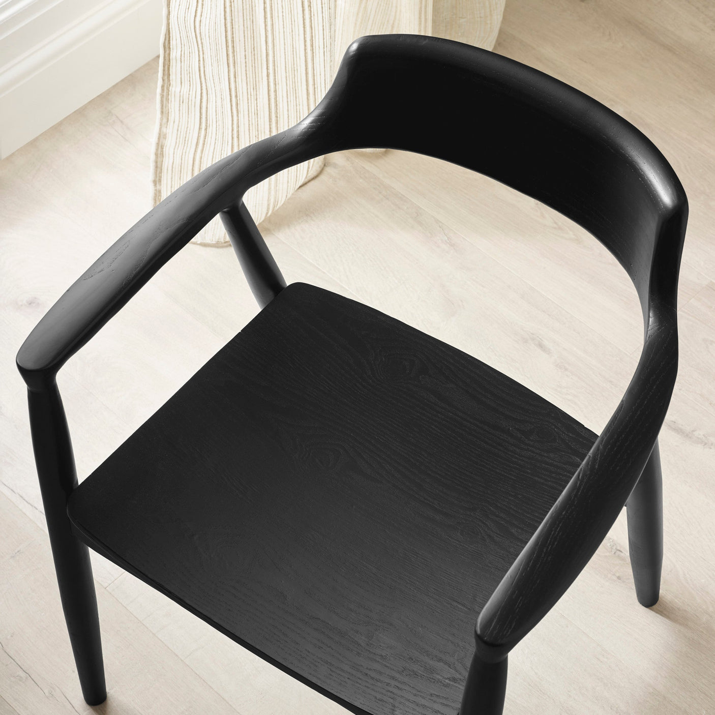 Close-up of black wooden dining chair with curved open backrest and armrests on light wood floor.