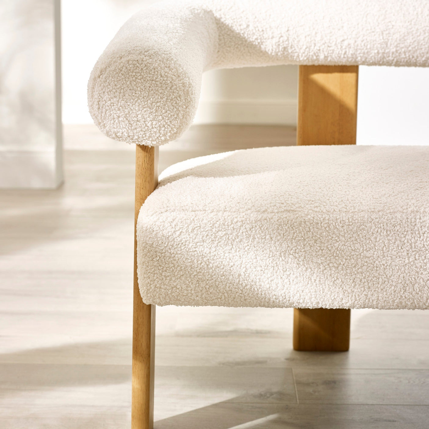 Close-up detail of cream boucle fabric seat and tubular curved backrest supported by wooden frame