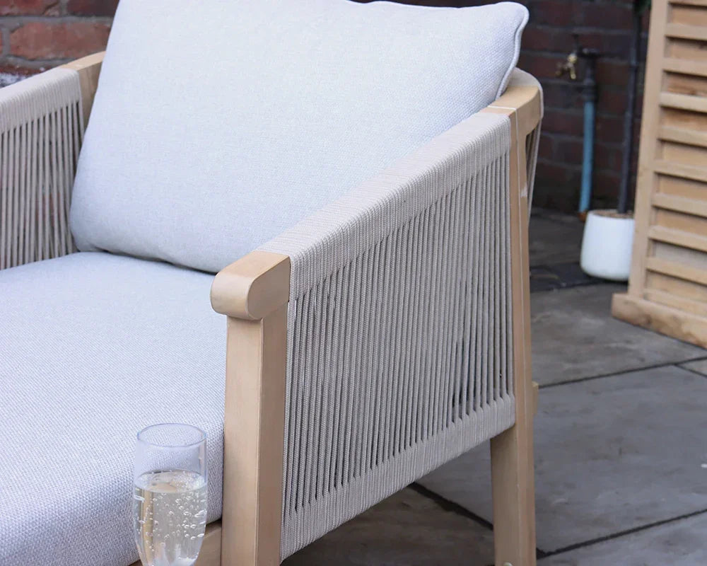 Light grey cushioned outdoor armchair with rope sides on patio, glass of sparkling drink on armrest