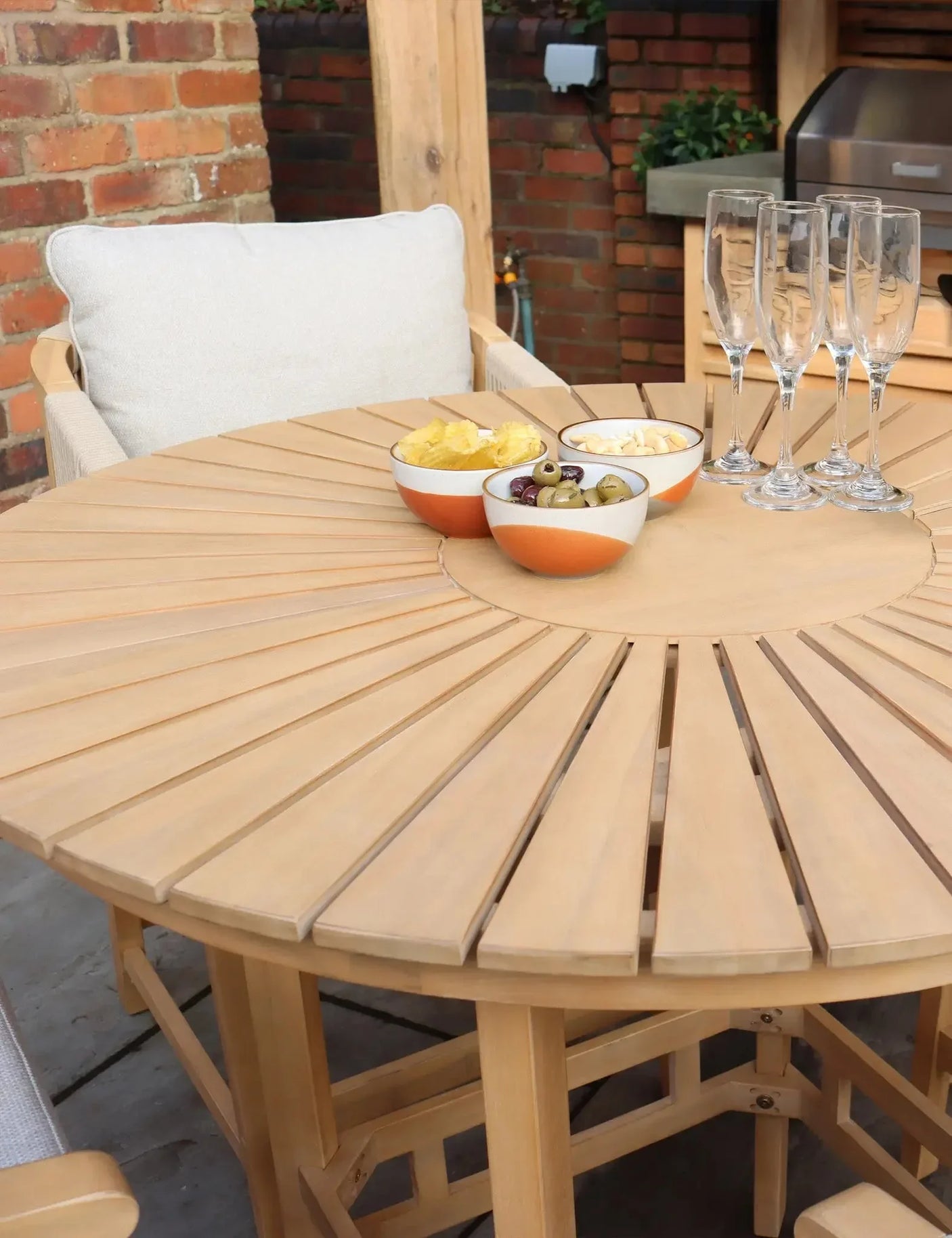 Wooden garden dining table with slatted top, cushioned chair, bowls and champagne flutes