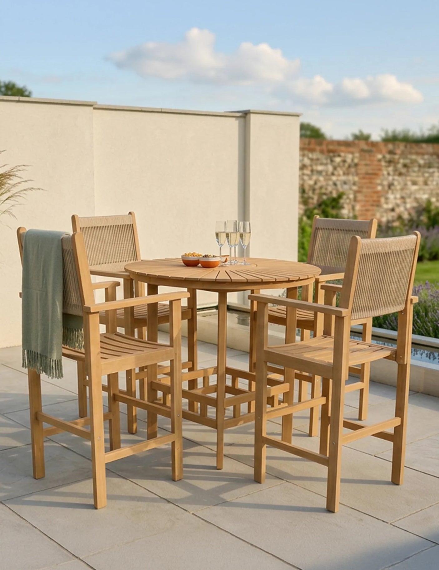 Wooden outdoor bar table with four matching bar chairs, set on a patio with drinks and snacks