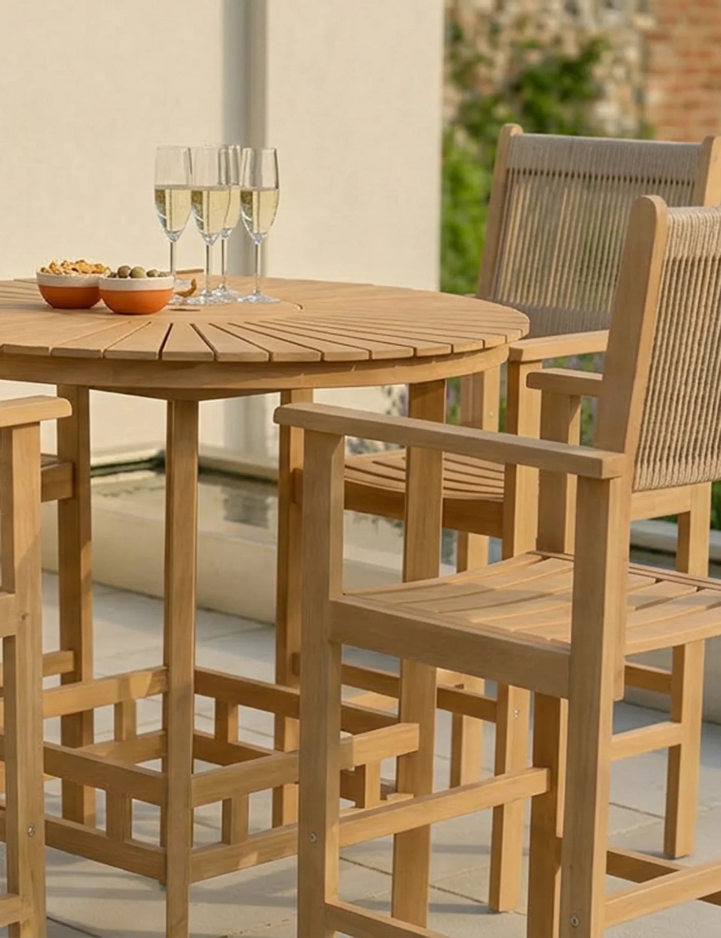 Wooden garden bar table set with high chairs, snacks, and drinks on sunlit patio