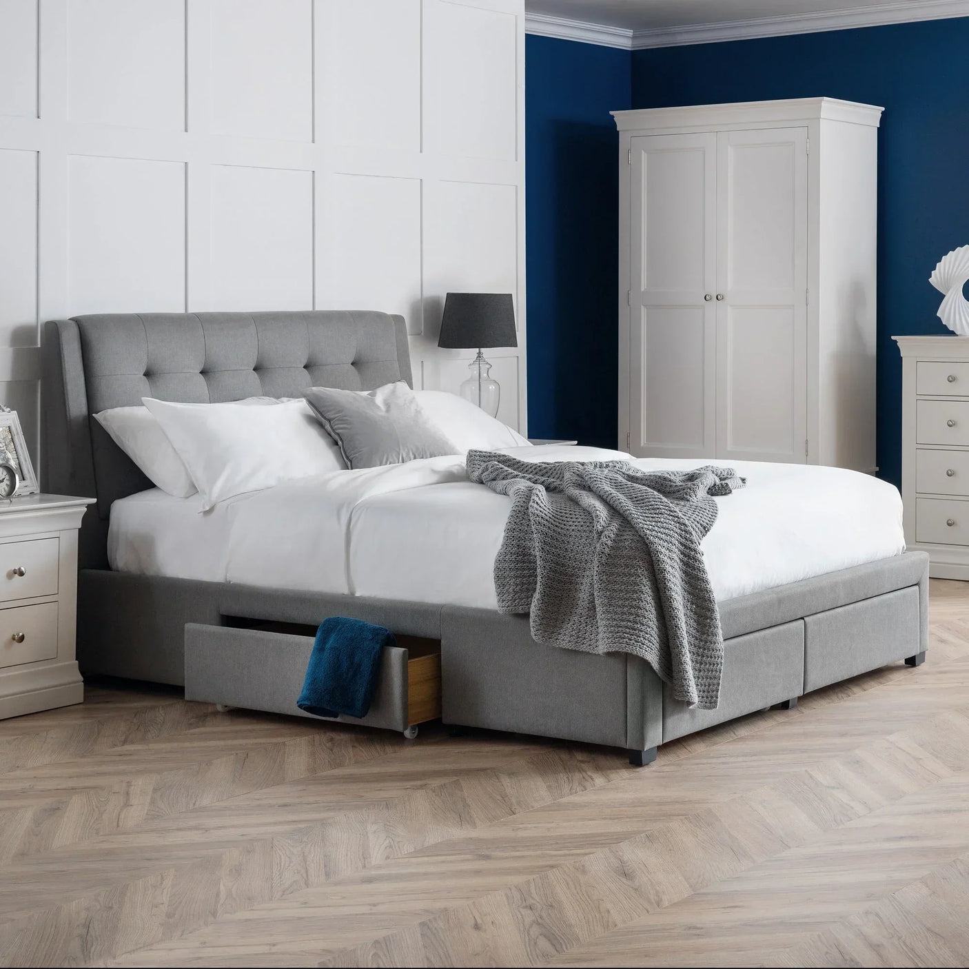 Grey double bed with four storage drawers in modern bedroom setting with white furniture