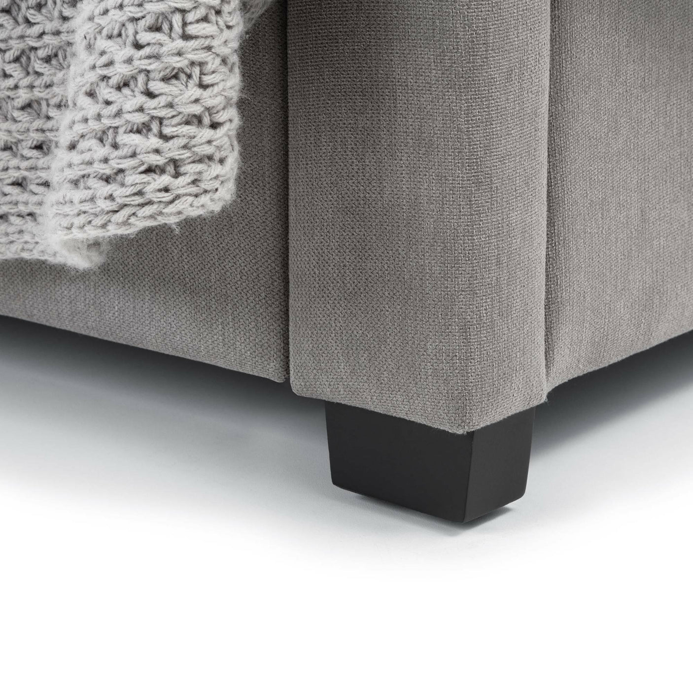 Grey fabric double bed corner with black wooden leg and textured knit throw detail