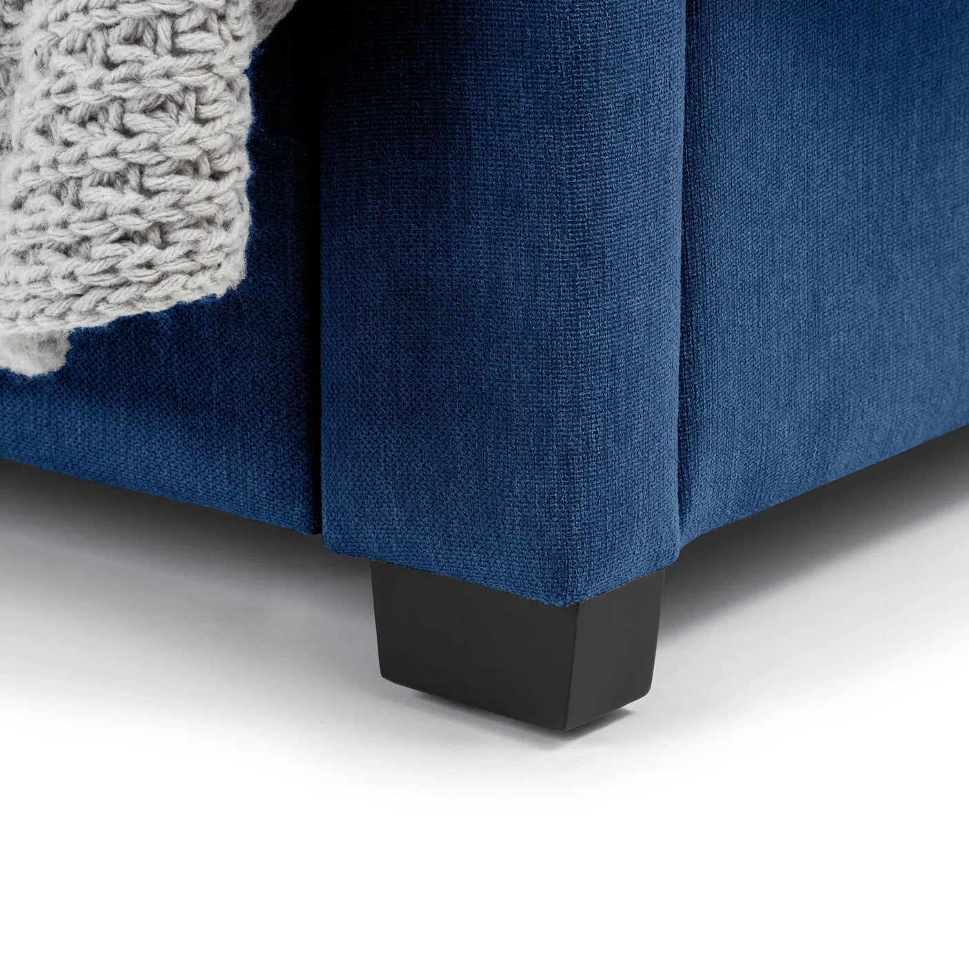 Close-up of blue double bed corner with fabric upholstery and black wooden leg