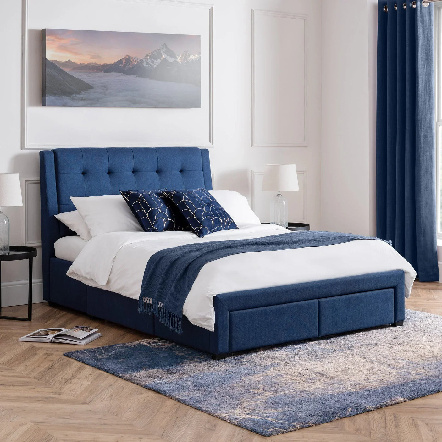 Blue upholstered double bed with four drawers in modern bedroom, matching blue curtains and rug