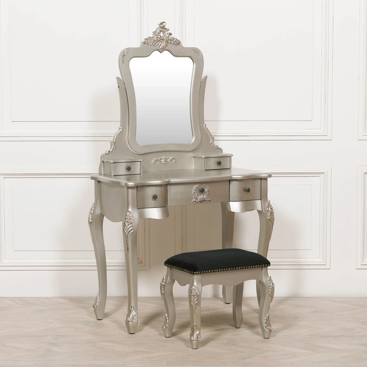 Silver dressing table with ornate mirror and black cushioned stool on wooden floor