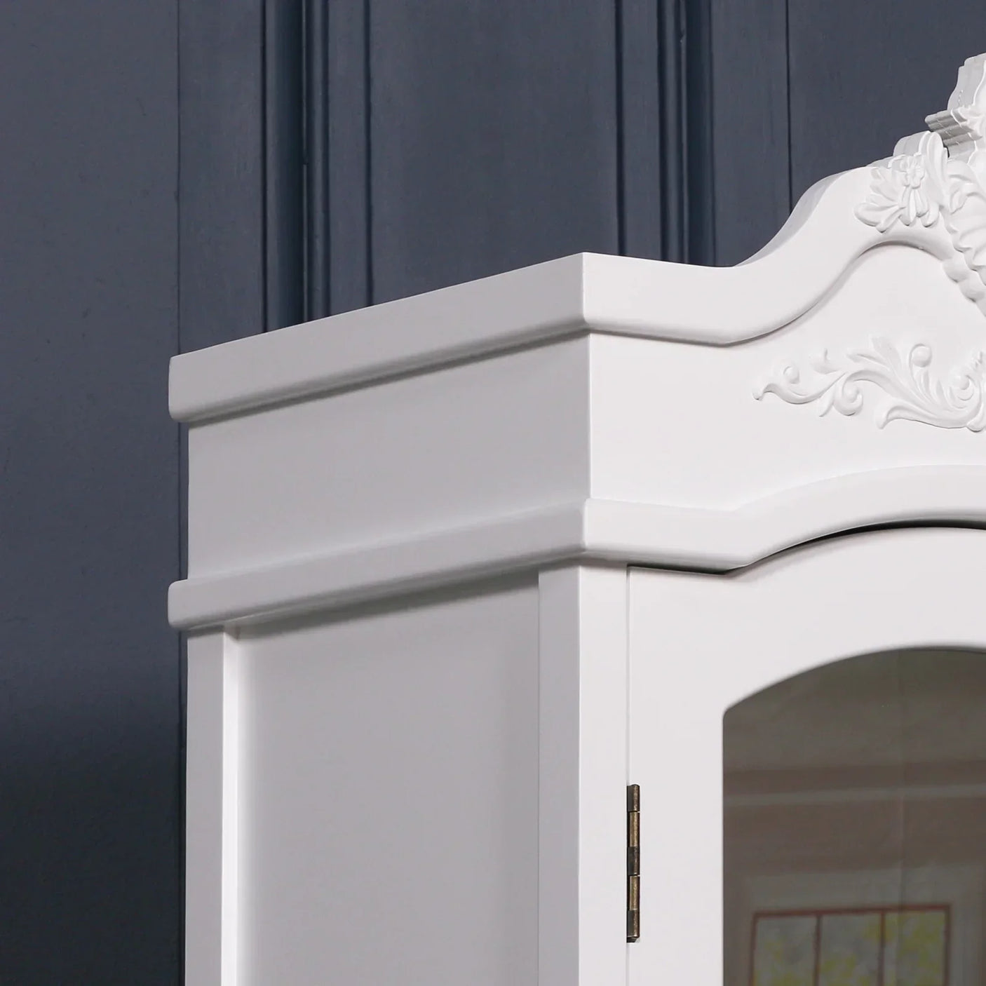 White wooden wardrobe top with ornate detailing against dark paneled wall