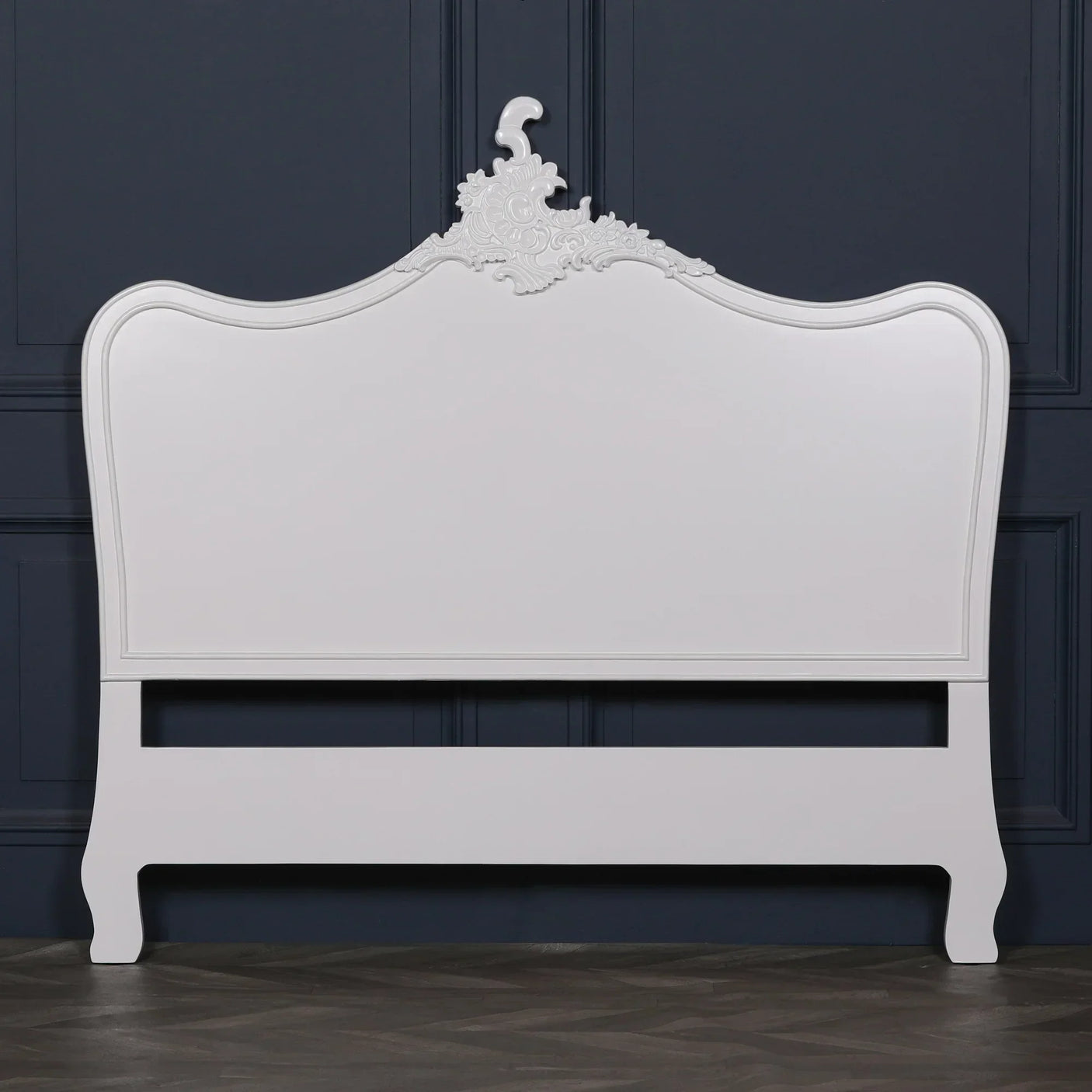 White wooden bed frame with ornate carved headboard against dark paneled wall