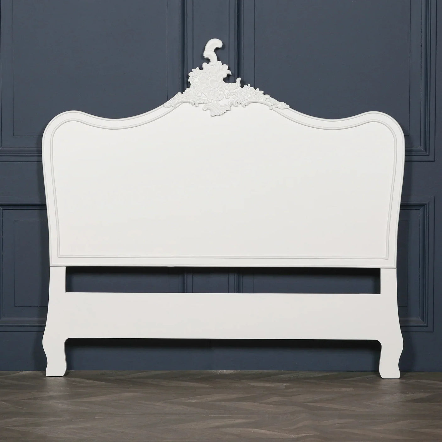 White wooden bed frame with ornate carved headboard against dark wall