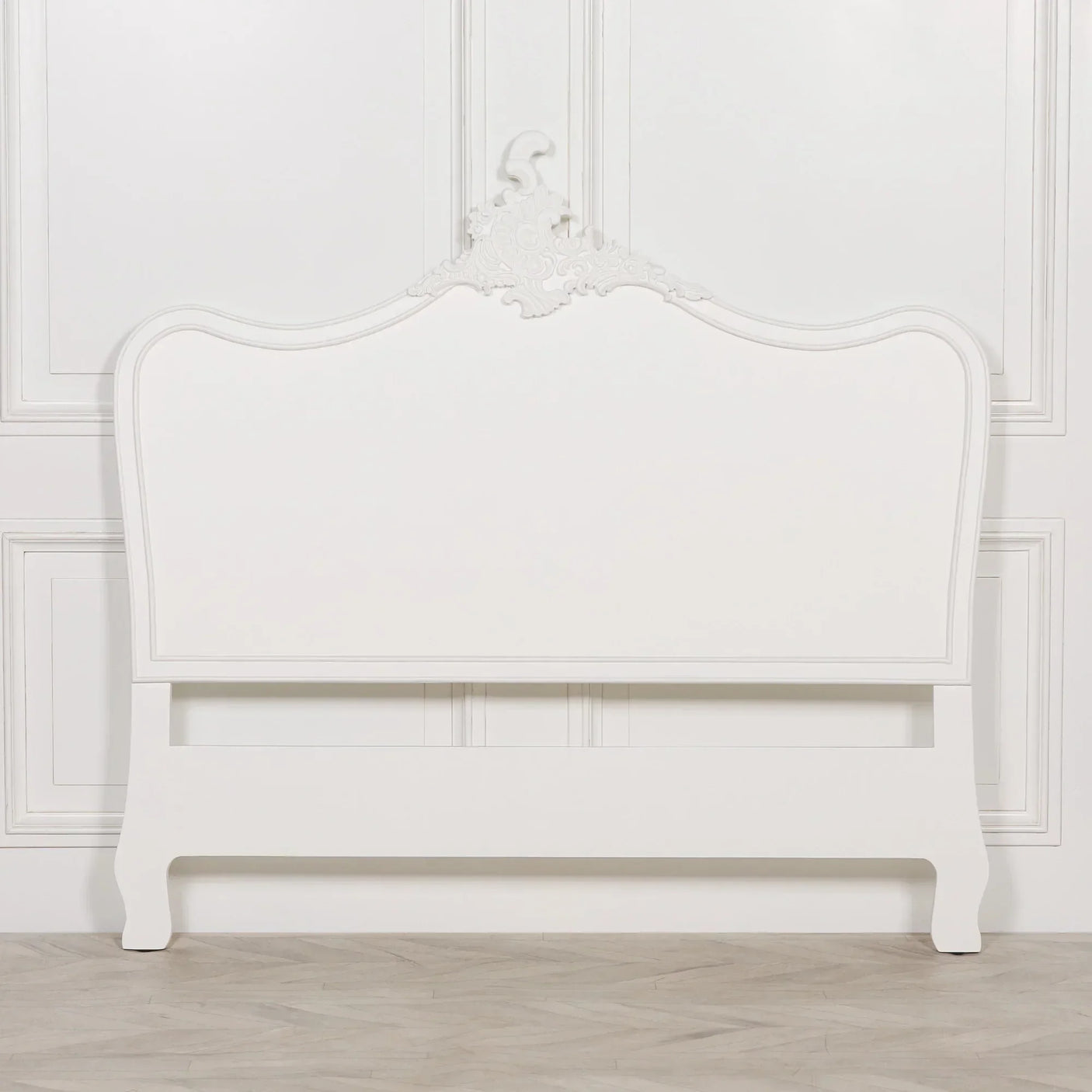 White wooden bed frame with ornate carved headboard against panelled wall