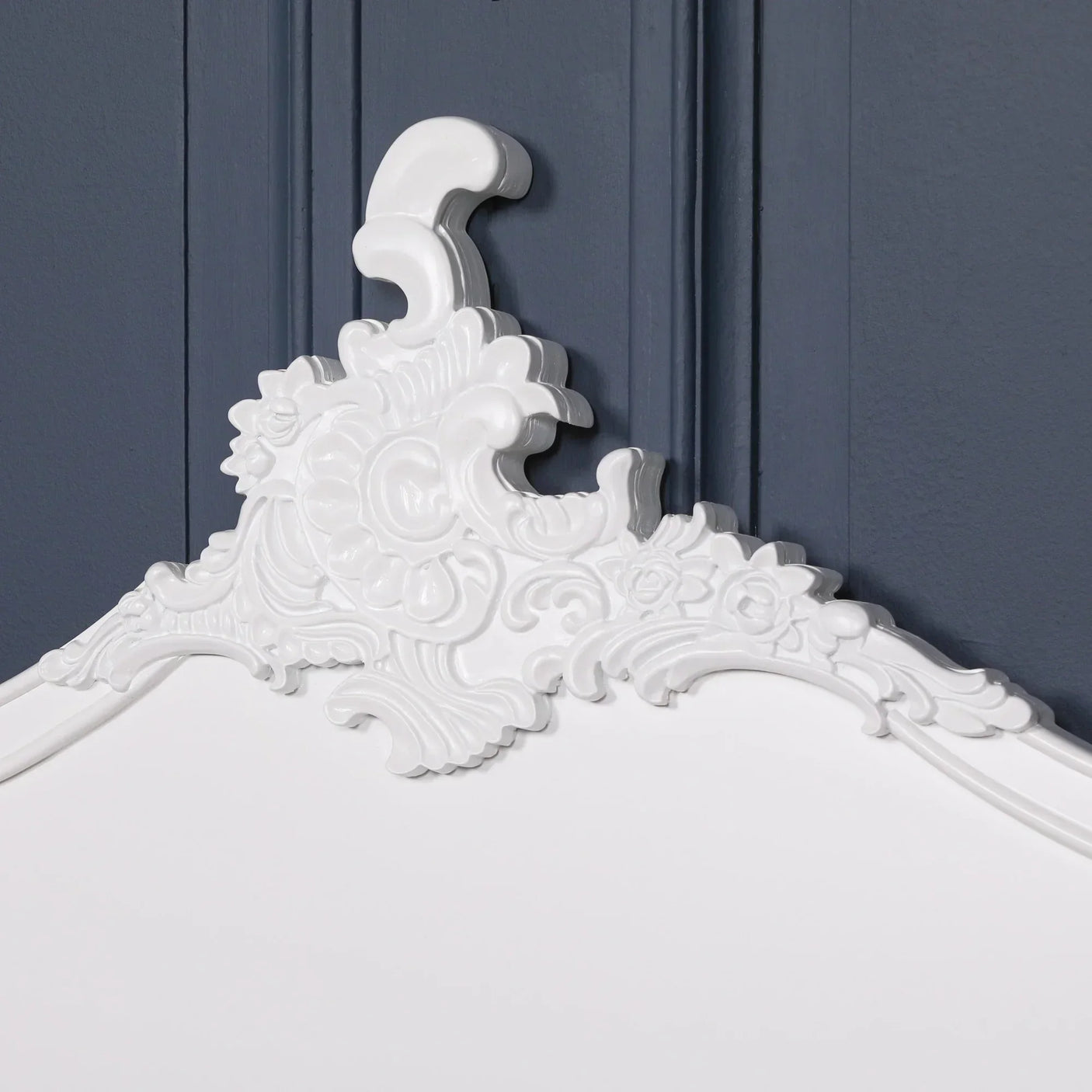 White wooden headboard with ornate carved floral detail against dark blue wall paneling
