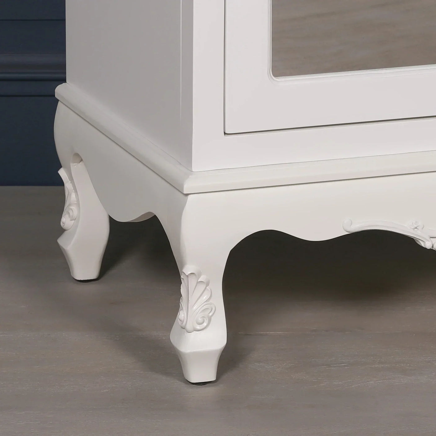White wooden cabinet with carved legs and scalloped detail on light wood floor