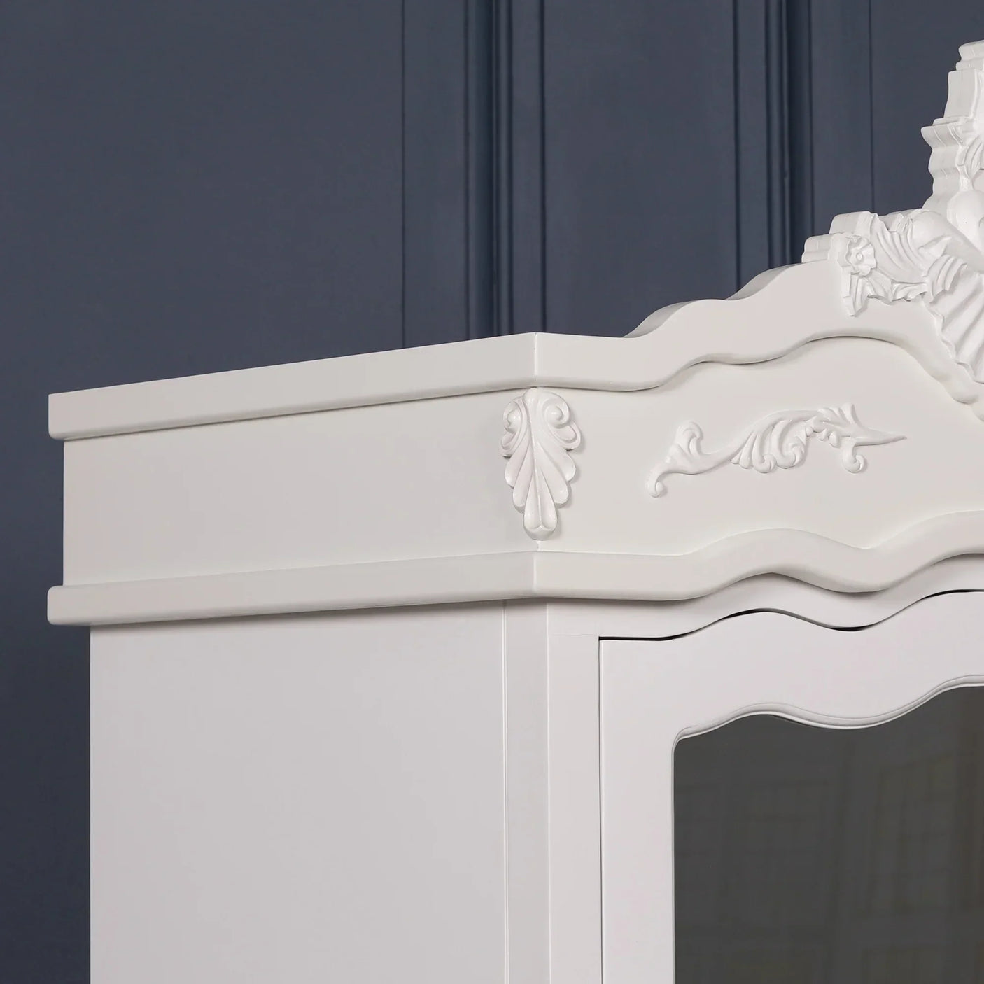 White wooden wardrobe with ornate carved detailing and curved top against a dark wall