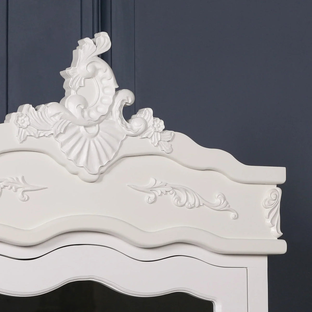 White wooden wardrobe top with ornate carved detailing and curved edges