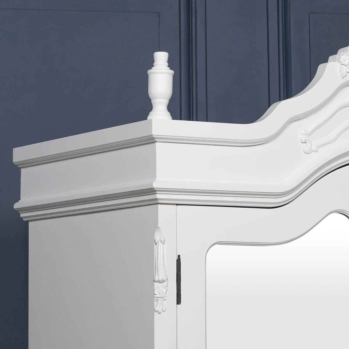 White wooden wardrobe corner with decorative trim and mirror door detail against blue wall