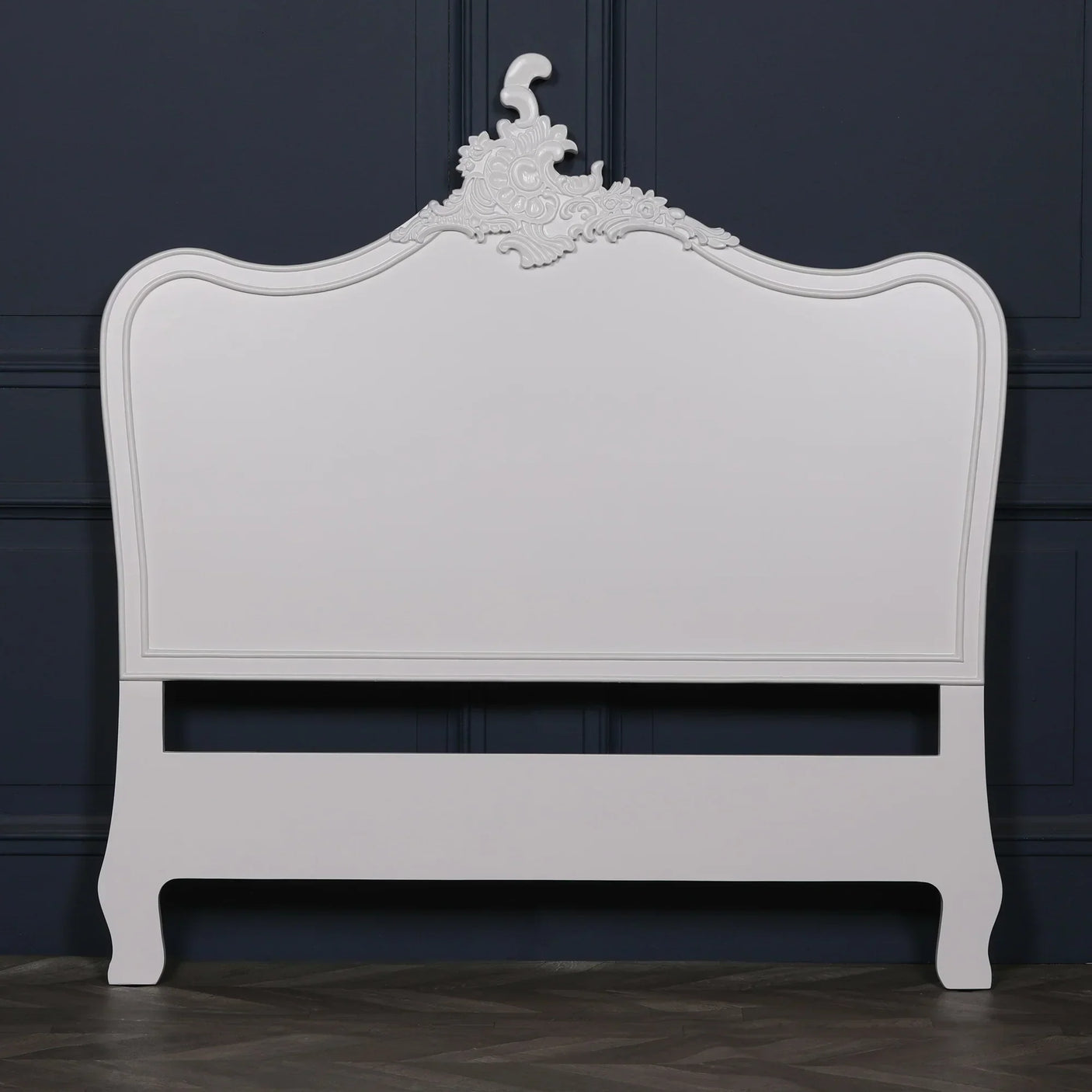 White wooden bed frame with ornate carved headboard against dark paneled wall