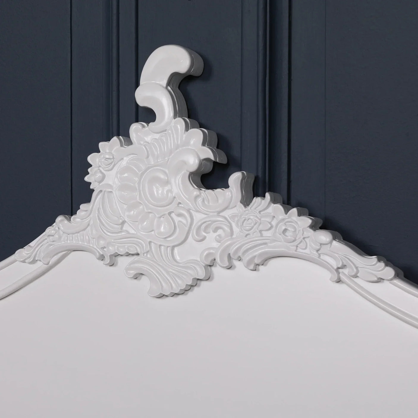 White ornate headboard with carved floral detail against dark blue wall