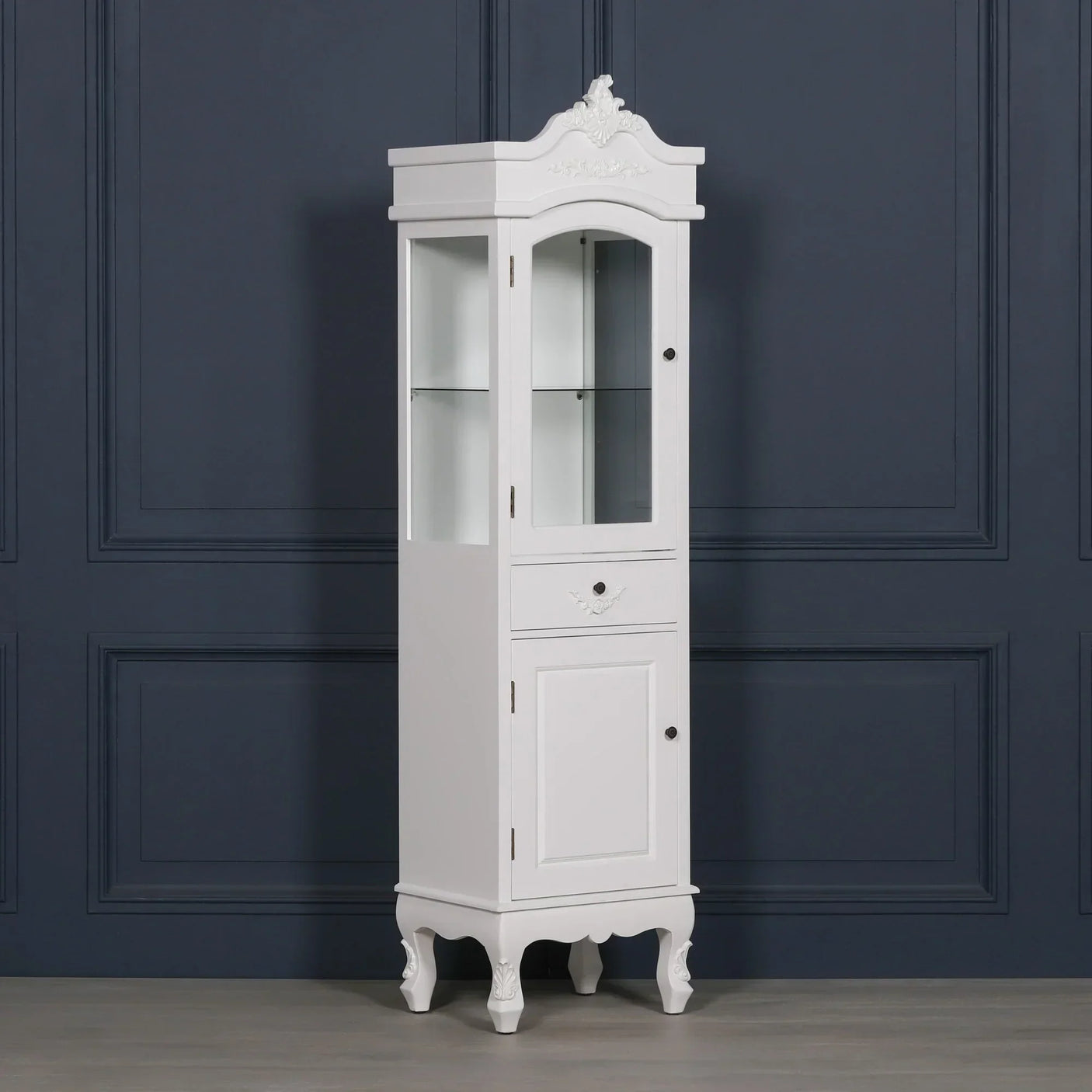 White display cabinet with glass door, drawer and ornate legs against dark wall