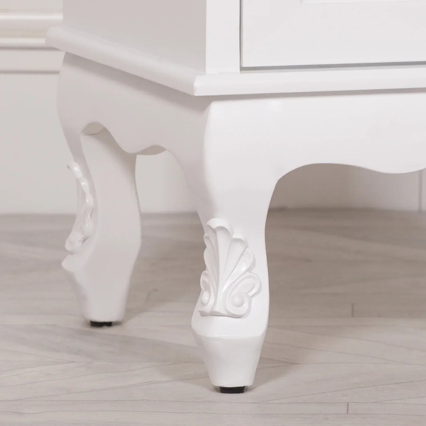 White wooden furniture leg with carved floral detail on light wood flooring