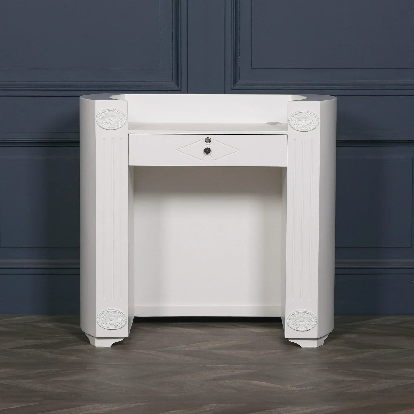 White console table with a single drawer and carved detailing, set against a dark blue wall