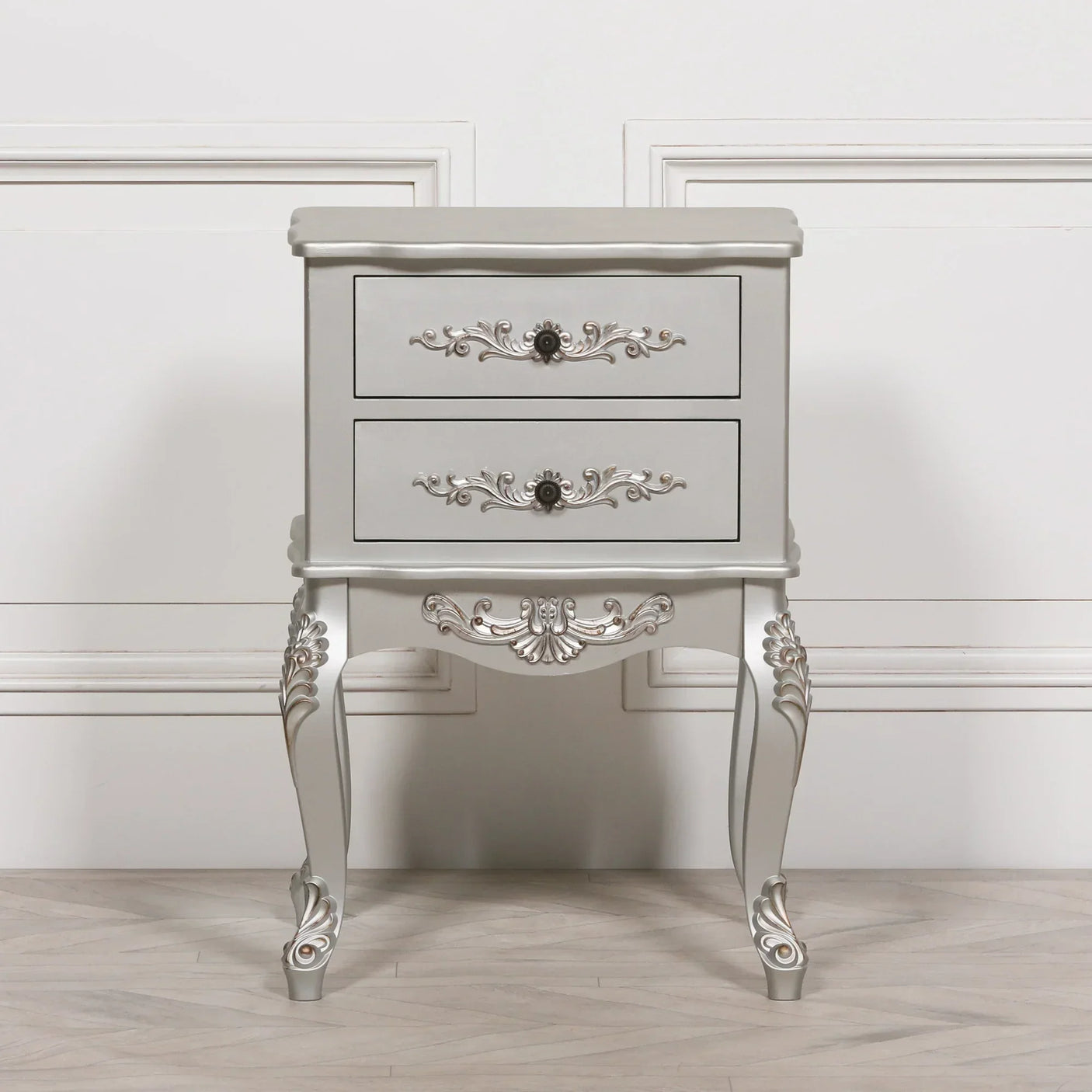 Silver bedside table with two drawers and ornate carved details on legs and drawer fronts