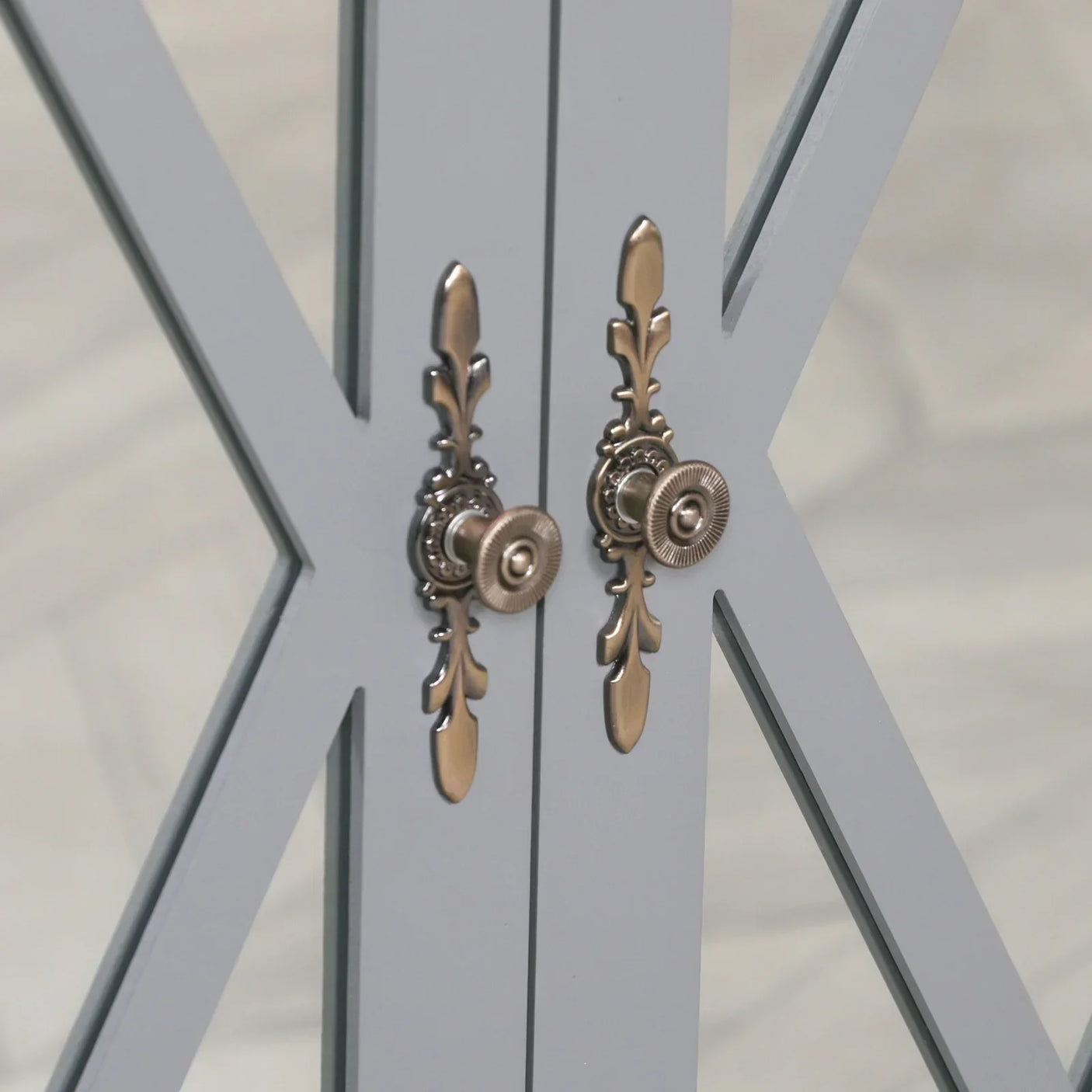 Close-up of grey cabinet doors with glass panels and ornate bronze handles