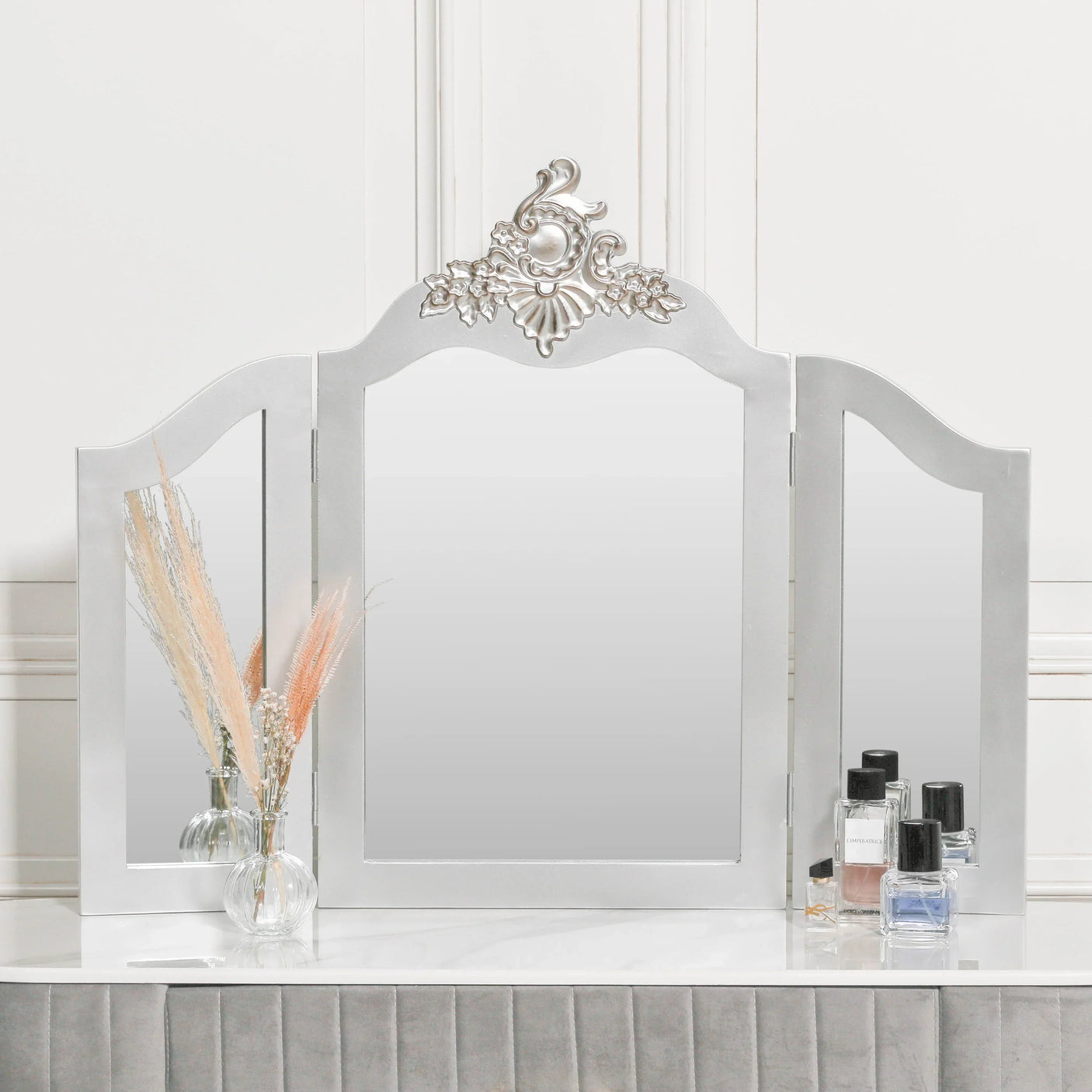 Silver dressing table mirror with three panels and ornate floral crest, perfumes on side