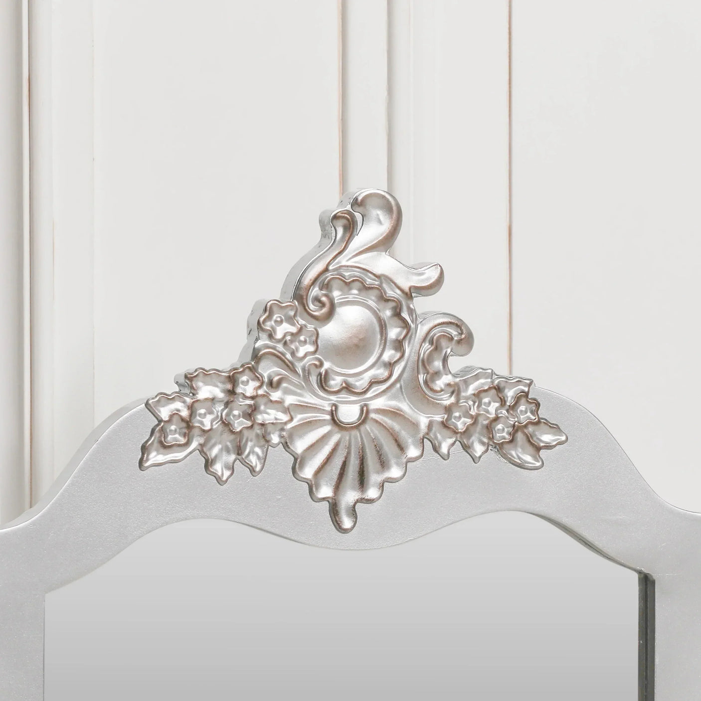 Silver ornate mirror frame with floral and shell detail against white panel background