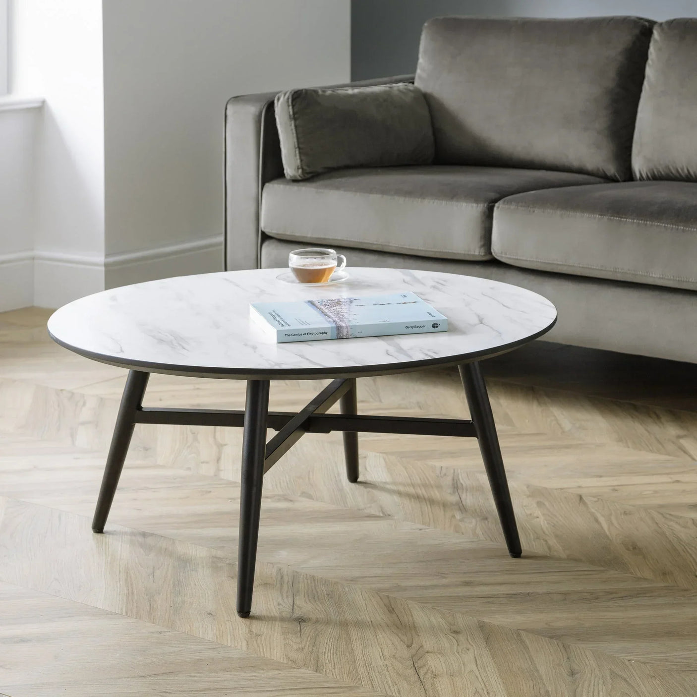 Marble top coffee table with black legs beside grey velvet sofa on wood flooring