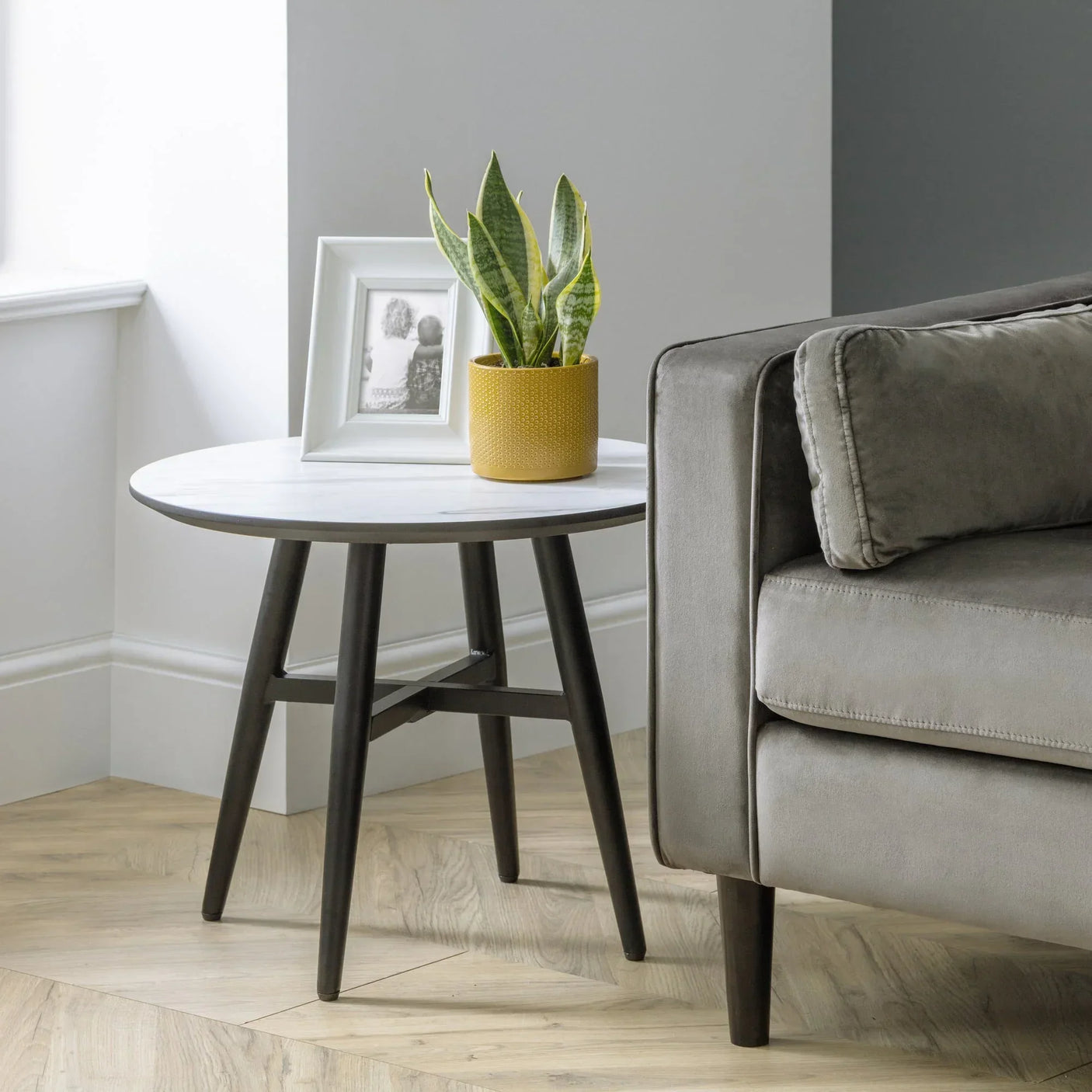 Round marble top lamp table with black legs beside grey sofa, plant and photo frame on top
